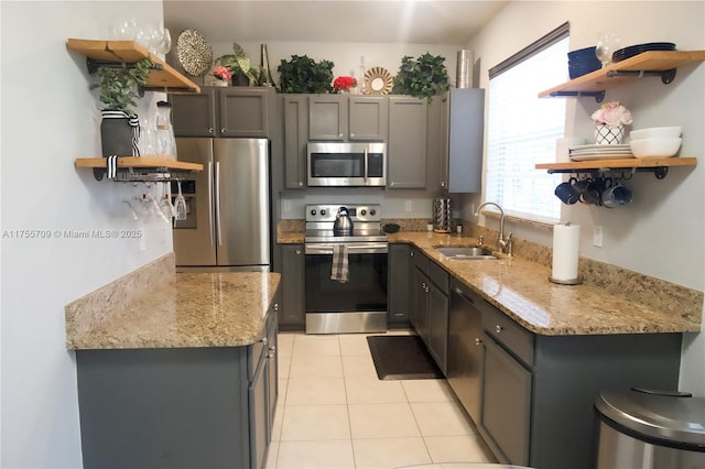 kitchen with light tile patterned flooring, a sink, appliances with stainless steel finishes, light stone countertops, and open shelves