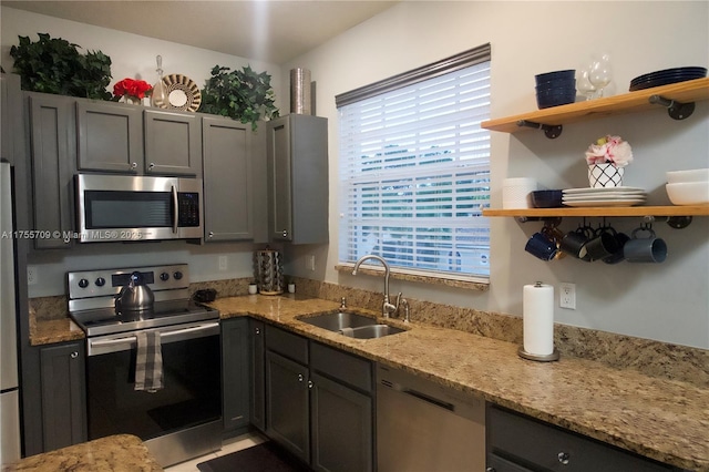 kitchen featuring open shelves, appliances with stainless steel finishes, a sink, and light stone counters