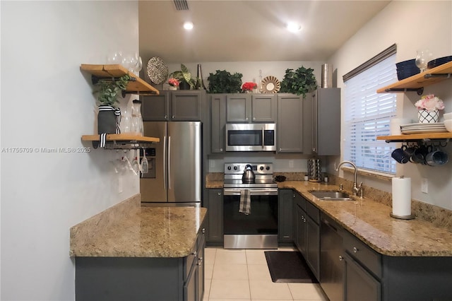 kitchen with light tile patterned floors, light stone counters, appliances with stainless steel finishes, open shelves, and a sink