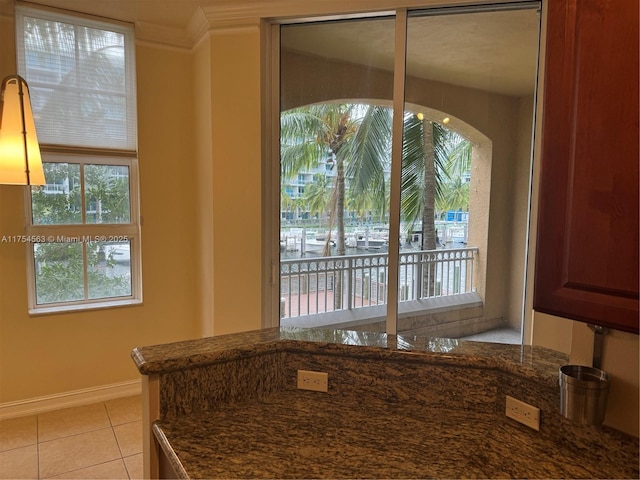 kitchen with light tile patterned floors, baseboards, dark stone counters, and crown molding