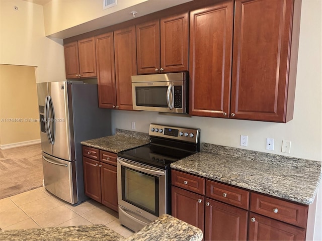 kitchen featuring light carpet, light tile patterned floors, appliances with stainless steel finishes, and dark stone countertops