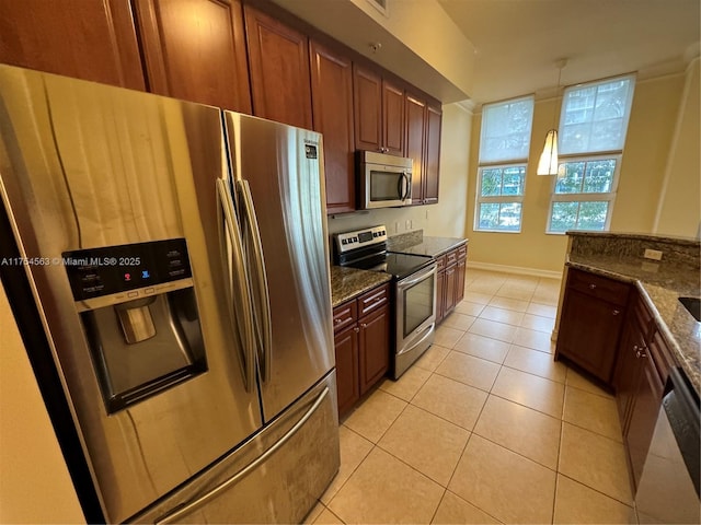 kitchen with baseboards, dark stone countertops, hanging light fixtures, stainless steel appliances, and light tile patterned flooring