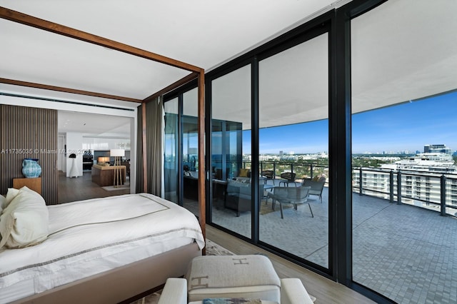 bedroom featuring access to exterior, a city view, wood finished floors, and floor to ceiling windows