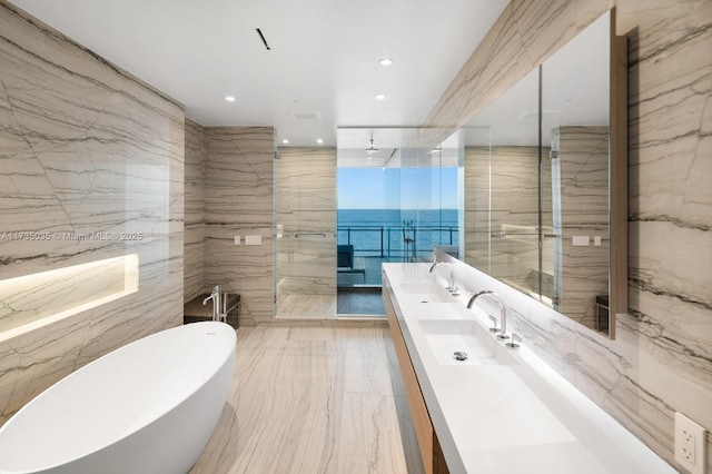 full bath featuring tile walls, double vanity, a freestanding bath, a sink, and stone wall