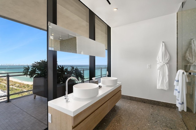 full bathroom with double vanity, a wall of windows, a water view, and baseboards