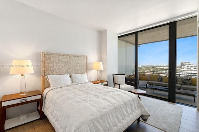 bedroom with floor to ceiling windows, a city view, and wood finished floors