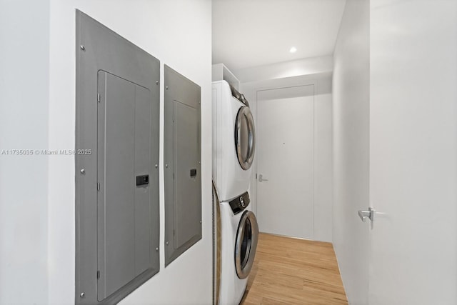 laundry area featuring stacked washer / drying machine, laundry area, electric panel, and light wood-style flooring