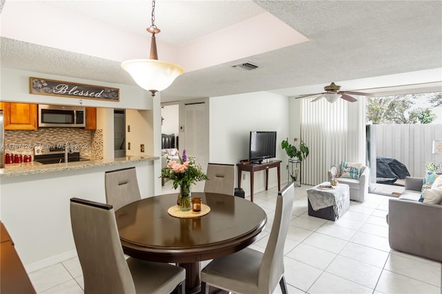 dining area with light tile patterned floors, a textured ceiling, visible vents, and a ceiling fan