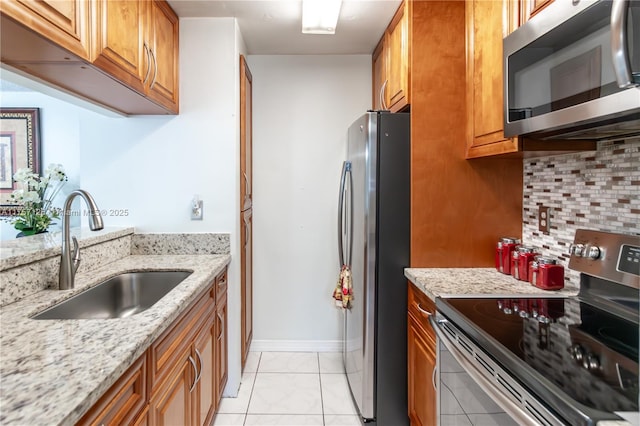 kitchen with brown cabinetry, a sink, light stone countertops, stainless steel appliances, and backsplash