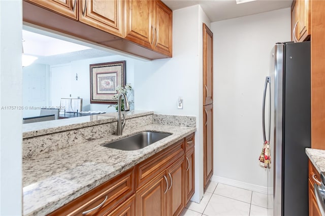 kitchen with light stone counters, freestanding refrigerator, brown cabinets, and a sink