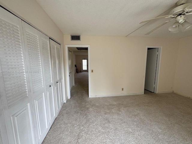 unfurnished bedroom with two closets, light colored carpet, visible vents, ceiling fan, and a textured ceiling