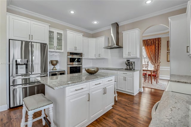 kitchen with stainless steel appliances, a kitchen island, dark wood-style floors, and wall chimney exhaust hood