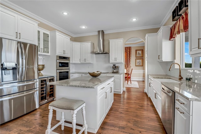 kitchen featuring white cabinetry, wine cooler, arched walkways, appliances with stainless steel finishes, and wall chimney range hood