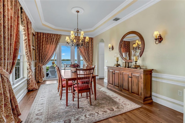 dining room featuring a tray ceiling, wood finished floors, arched walkways, an inviting chandelier, and crown molding