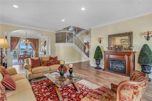 living area with wood finished floors, arched walkways, ornamental molding, stairs, and a glass covered fireplace