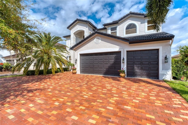 mediterranean / spanish-style house with decorative driveway, a garage, stucco siding, and a tiled roof