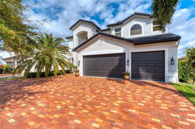 view of front of house featuring stucco siding, an attached garage, a tile roof, and decorative driveway