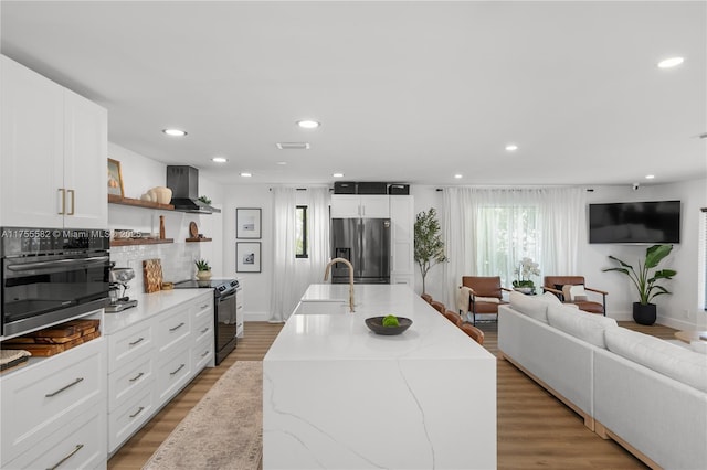 kitchen featuring stainless steel fridge with ice dispenser, black electric range oven, wall oven, a sink, and wall chimney exhaust hood