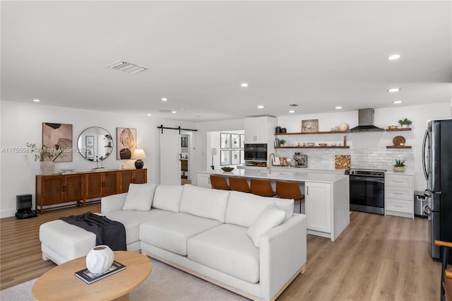 living area featuring a barn door, visible vents, light wood-style flooring, and recessed lighting