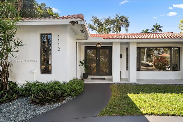 view of exterior entry with french doors, a yard, a tiled roof, and stucco siding