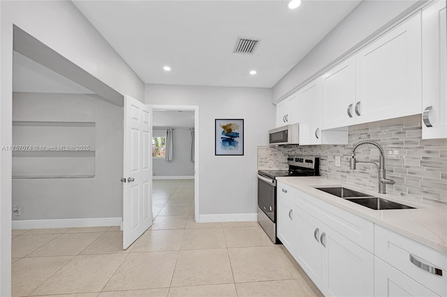 kitchen with light tile patterned floors, a sink, white cabinets, tasteful backsplash, and stainless steel range with electric stovetop