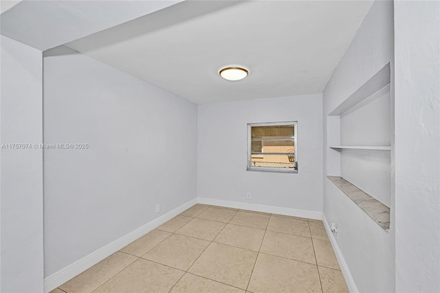 empty room with light tile patterned floors, built in shelves, and baseboards