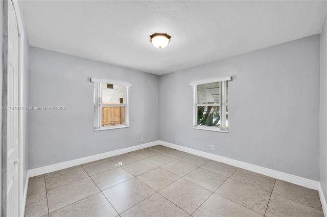 tiled spare room featuring a healthy amount of sunlight and baseboards