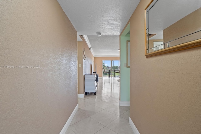 corridor featuring a textured ceiling, a textured wall, light tile patterned floors, and baseboards