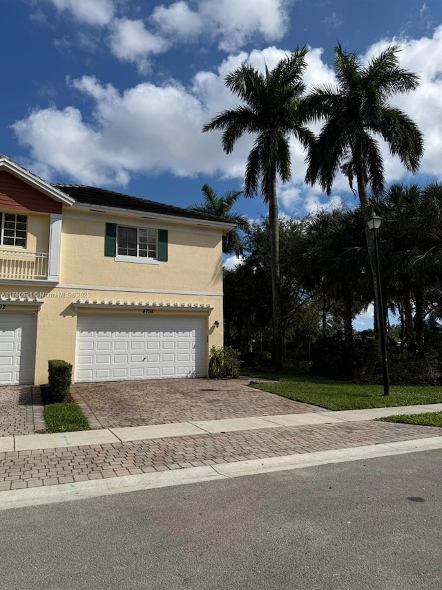 view of front of house with decorative driveway, an attached garage, and stucco siding