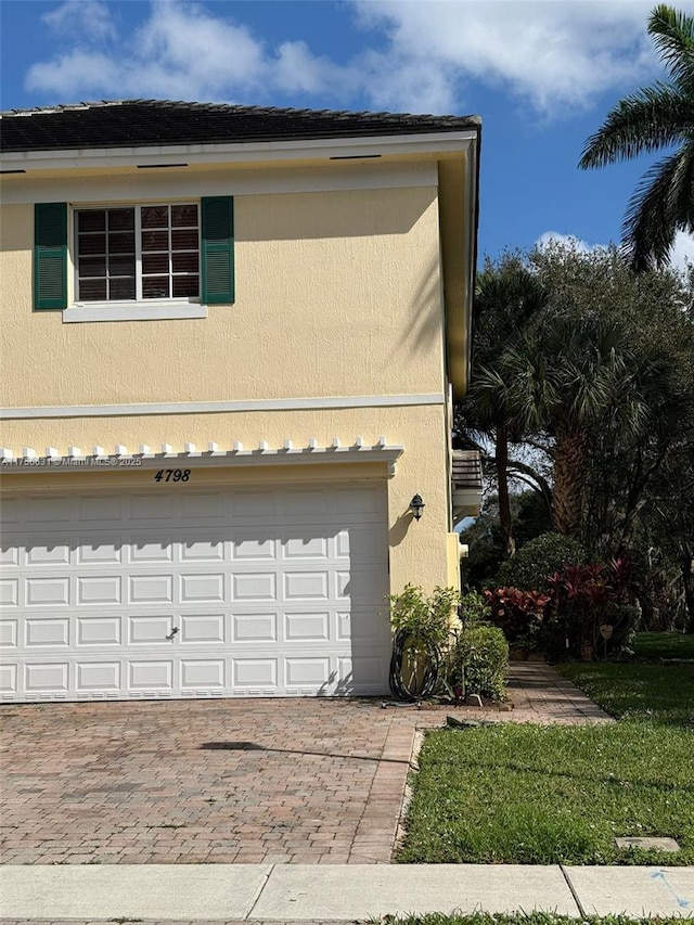 view of side of property with a garage, decorative driveway, and stucco siding