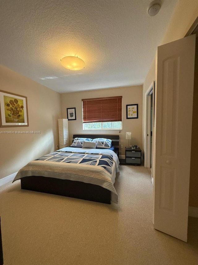 bedroom featuring a textured ceiling, baseboards, and light colored carpet