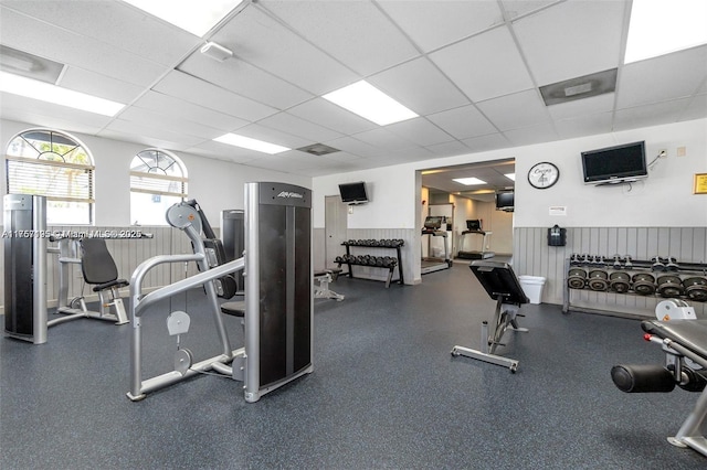 gym featuring a paneled ceiling and a wainscoted wall