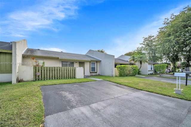 view of front of property featuring fence, driveway, a front lawn, and stucco siding