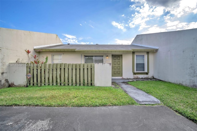 view of front of home featuring fence, a front lawn, and stucco siding