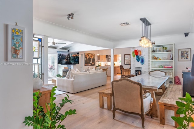 dining space with light wood finished floors, a fireplace, visible vents, and ceiling fan with notable chandelier