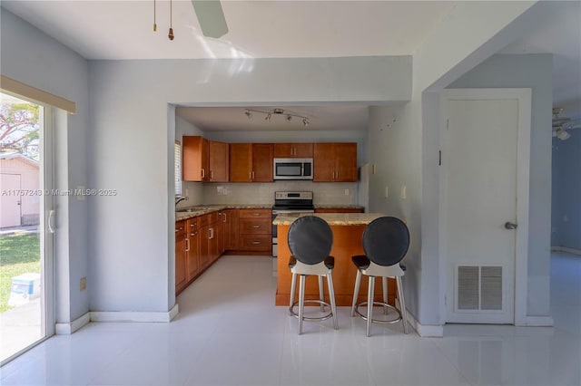 kitchen featuring visible vents, a kitchen bar, backsplash, appliances with stainless steel finishes, and brown cabinetry