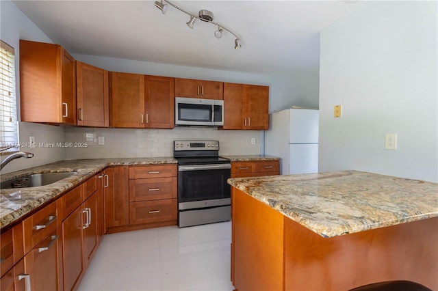 kitchen with light stone counters, decorative backsplash, brown cabinets, stainless steel appliances, and a sink