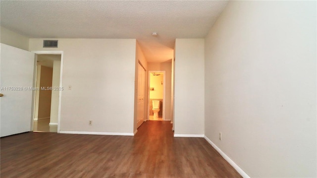 unfurnished room with a textured ceiling, wood finished floors, visible vents, and baseboards