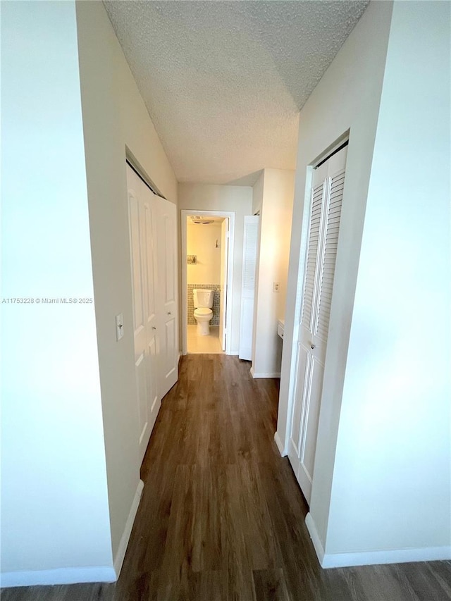 hallway featuring dark wood finished floors, a textured ceiling, and baseboards