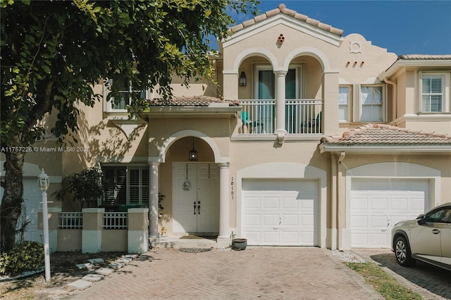 mediterranean / spanish home with a balcony, driveway, an attached garage, stucco siding, and a tiled roof