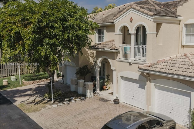 mediterranean / spanish house with a balcony, fence, stucco siding, a tiled roof, and decorative driveway