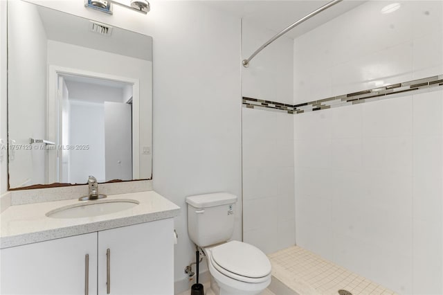 bathroom with toilet, visible vents, a tile shower, and vanity