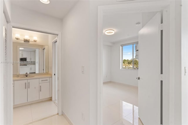 hall featuring light tile patterned flooring, a sink, and baseboards