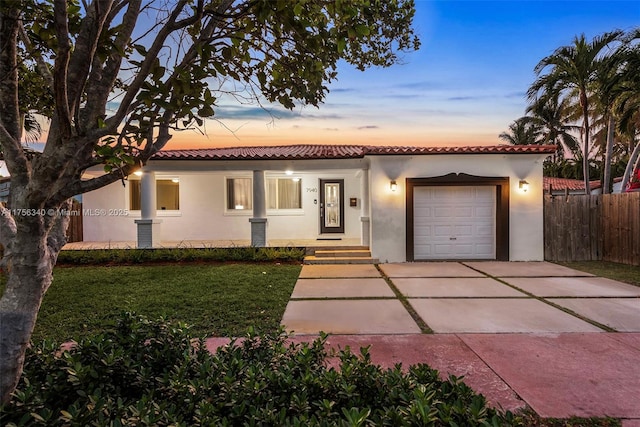 mediterranean / spanish house with an attached garage, a tile roof, fence, concrete driveway, and stucco siding