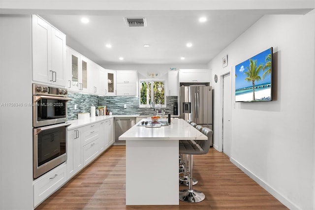 kitchen featuring a kitchen breakfast bar, tasteful backsplash, a kitchen island with sink, light countertops, and stainless steel appliances