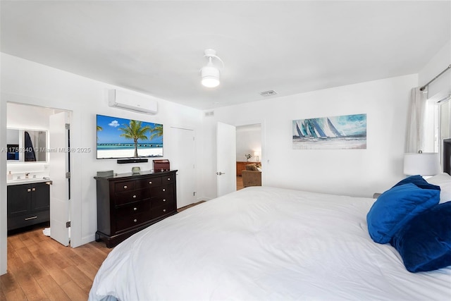 bedroom featuring ensuite bath, visible vents, a wall mounted AC, a sink, and light wood finished floors