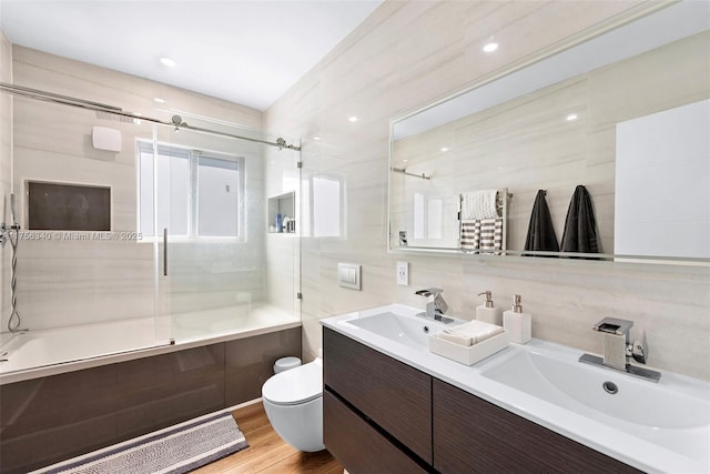 full bath with toilet, tile walls, a sink, and shower / bath combination with glass door