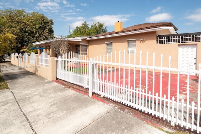 exterior space with a fenced front yard, a chimney, a gate, and stucco siding