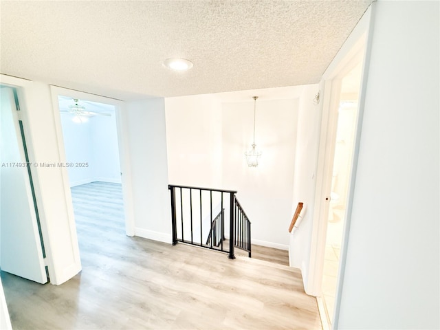 interior space featuring an upstairs landing, baseboards, light wood finished floors, and a textured ceiling