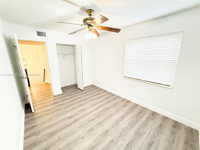 unfurnished bedroom with light wood finished floors, visible vents, a textured ceiling, and a closet